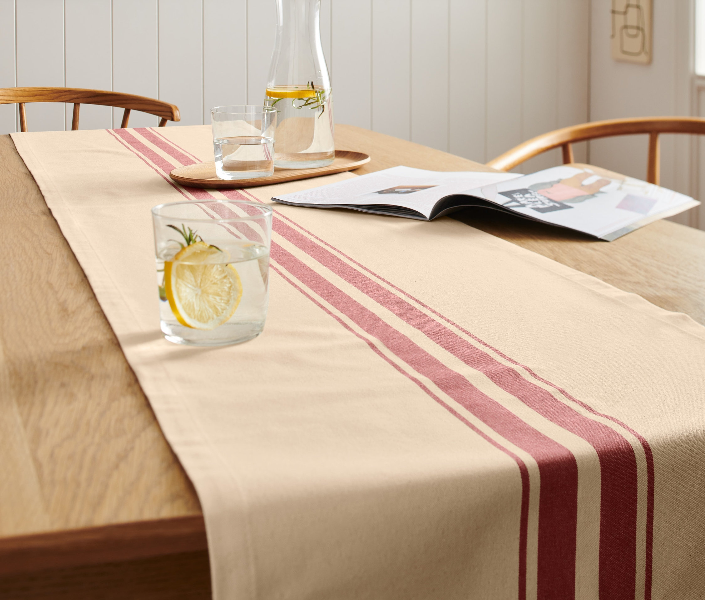 Csíkos asztali futó egy fa asztalon. Elöl egy pohár víz citrommal.