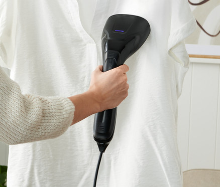 Egy nő egy gőzkefét használ egy vállfán lógó fehér inghez.