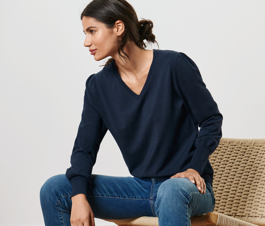 Nő ül egy széken, kék, női finomkötésű pulóvert és farmert visel.