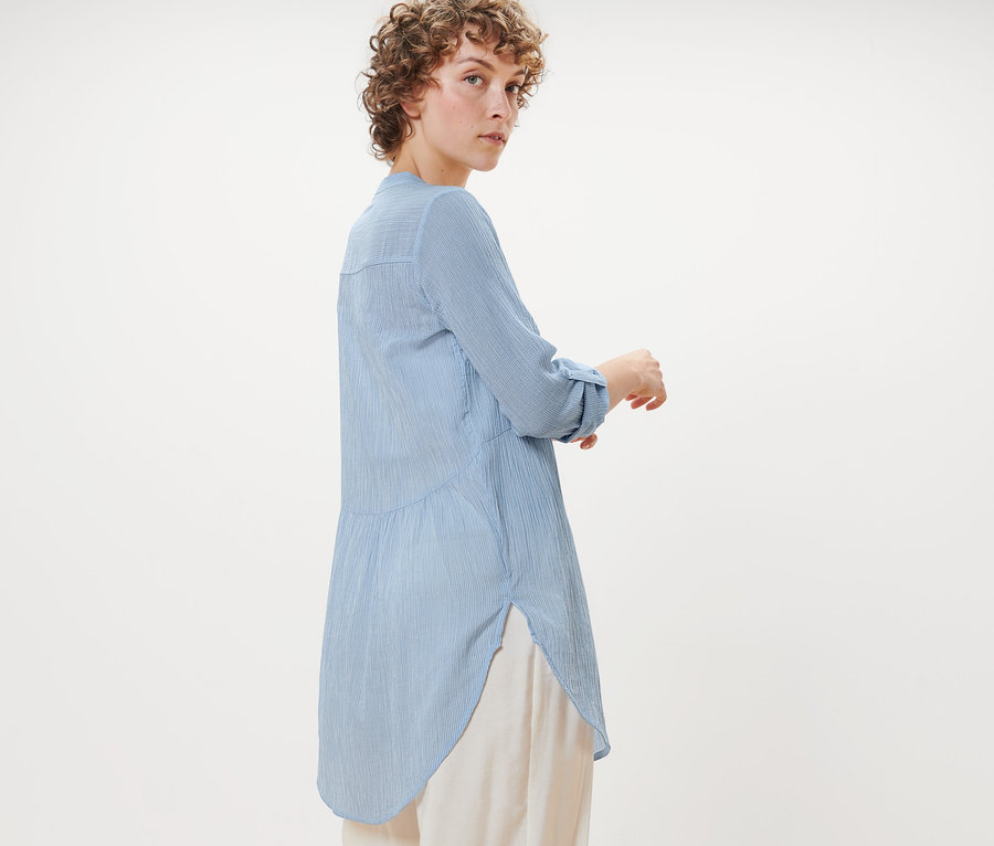 Nő pózol csíkos hosszú blúzban.