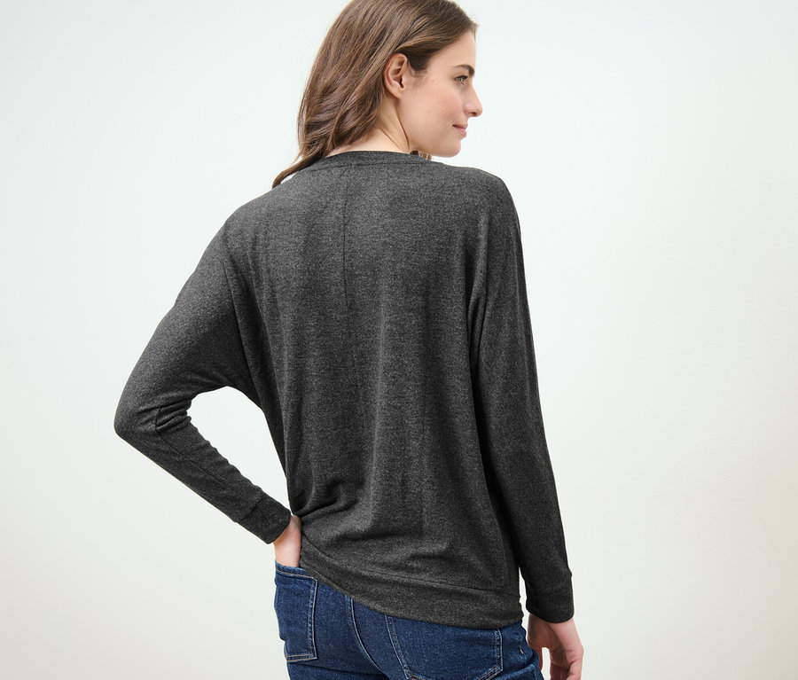 Nő visel egy melírozott sötétszürke denevérujjú felsőt és farmert.