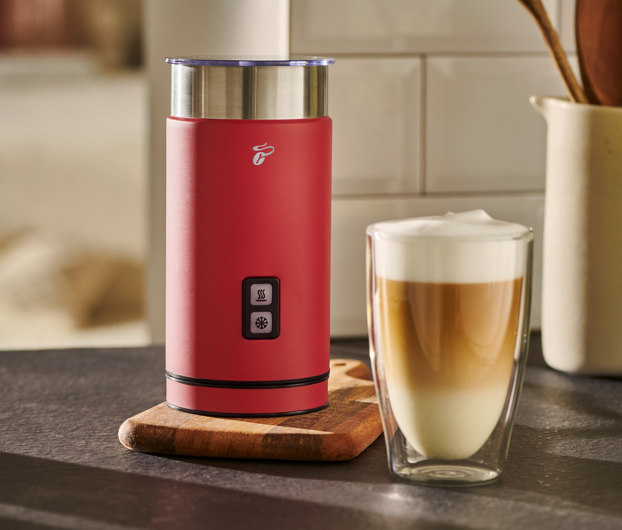 Egy piros elektromos tejhabosító áll egy pohár tejeskávé mellett.