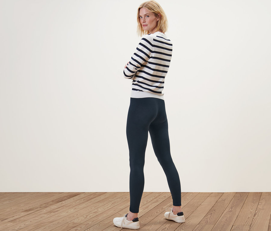 Nő pózol leggingsben és csíkos pulóverben.
