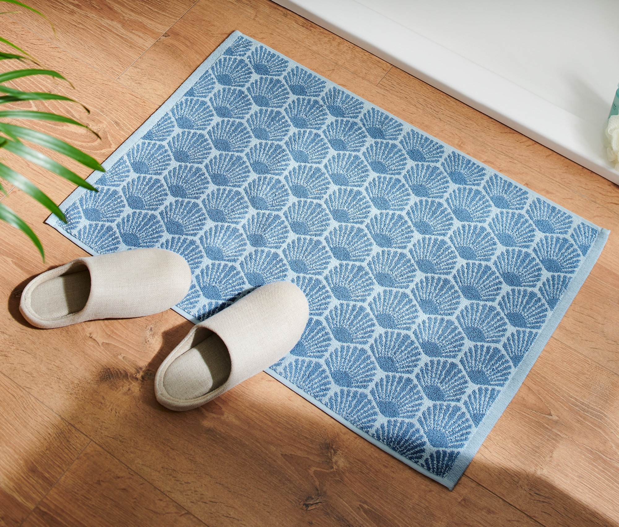 A fapadlón egy kék Kagylómintás fürdőszobai kilépő és egy pár bézs papucs látható.