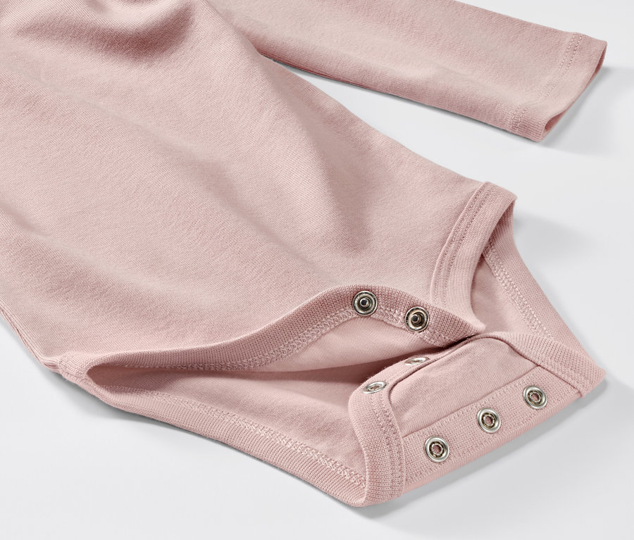 Egy rózsaszín, hosszú ujjú baba body közelképe egy ötdarabos szettből.