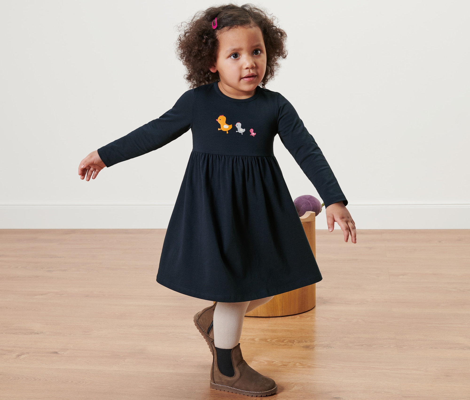 Kislány pózol kék hosszú ujjú jerseyruhában madár mintákkal, barna csizmával.