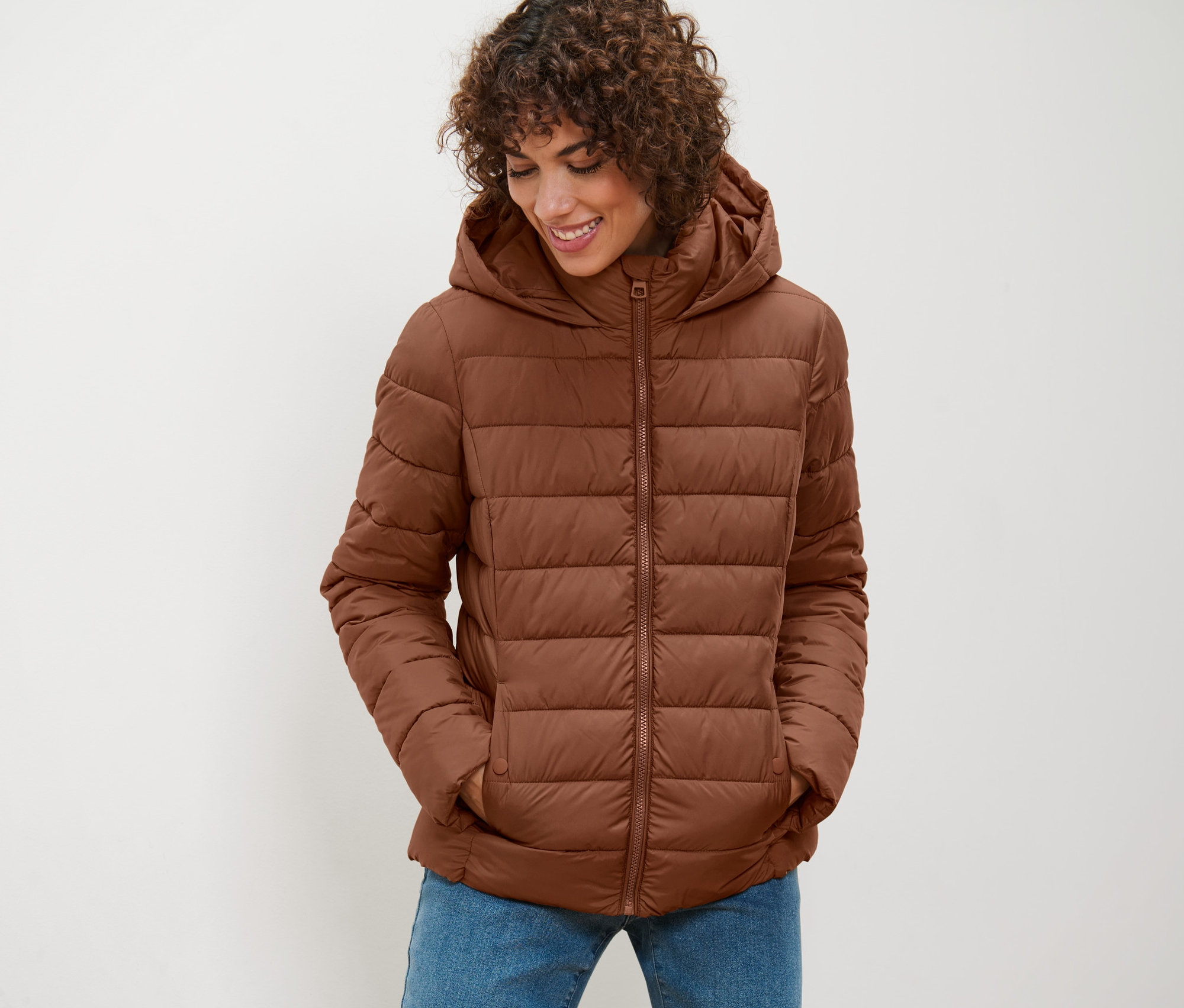 Nő visel barna, steppelt dzsekit kapucnival, és lefelé néz.