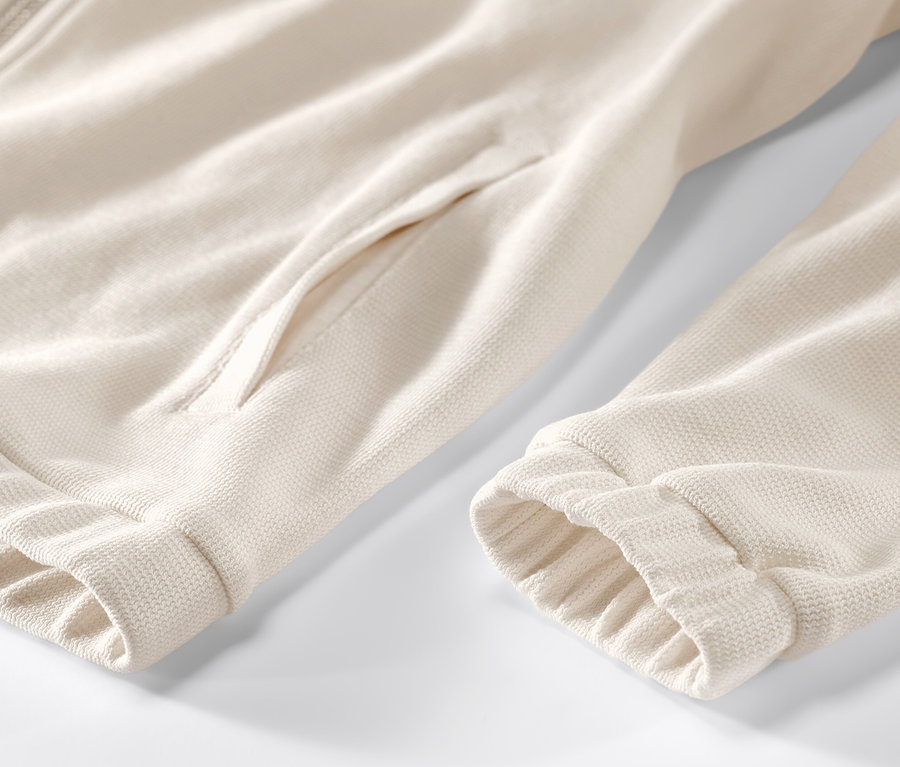 Egy krémszínű, cipzáras, zsebes szabadidőfelső részlete.