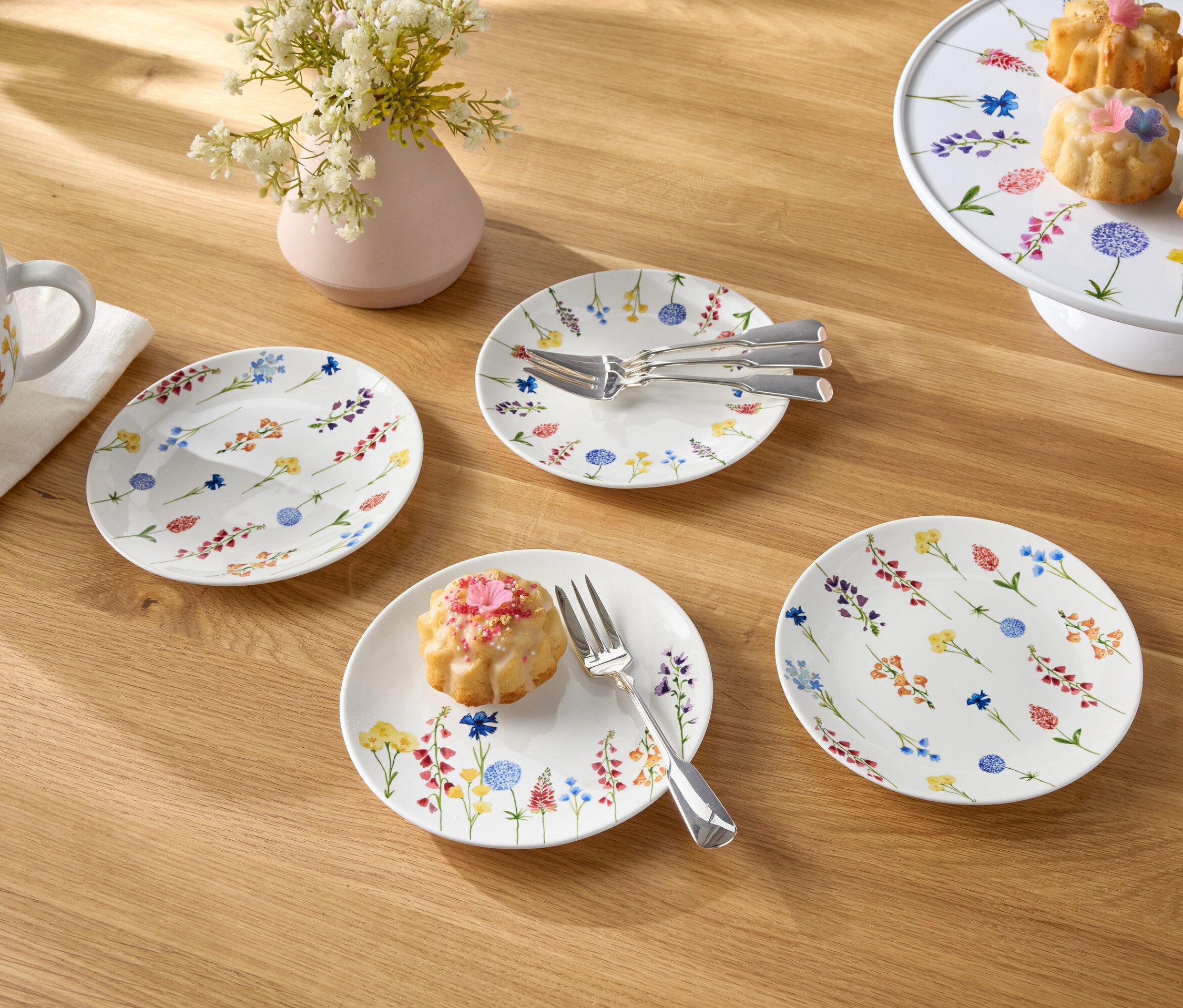 Egy fa asztalon egy csésze kávé, egy váza virág, tányérok és kis sütemények találhatók.