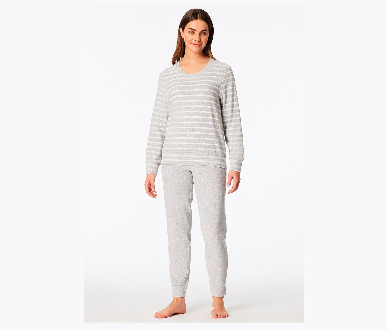 Egy nő áll mezítláb, szürke-fehér csíkos pizsamában.