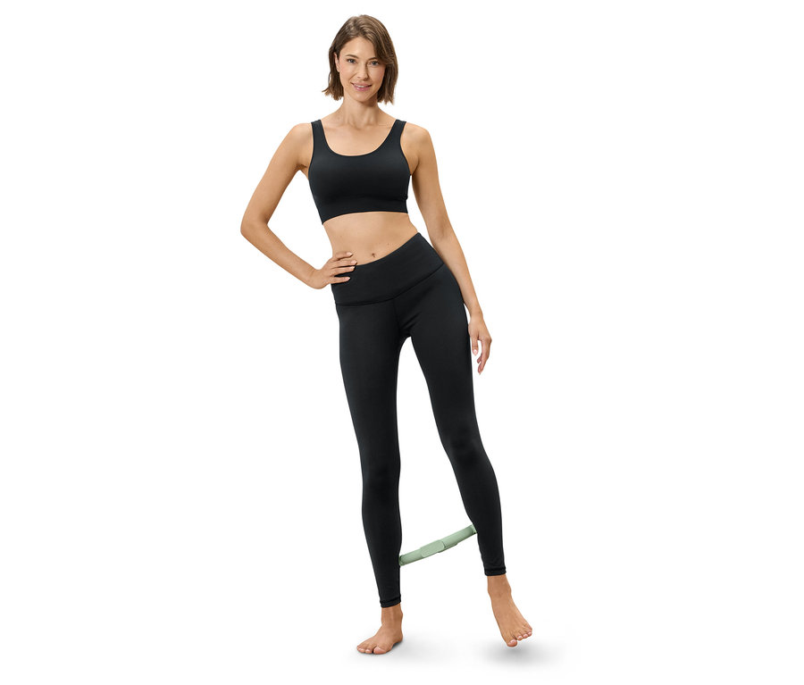 Nő edzést végez gumiszalaggal a lábán, sportmelltartót és leggingset visel.