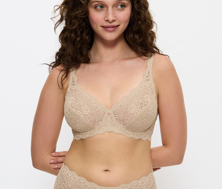 Barna hajú nő pózol bézs csipkés melltartóban és bugyiban.