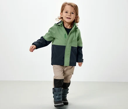 Egy fiúgyermek zöld/sötétkék softshell dzsekit visel.