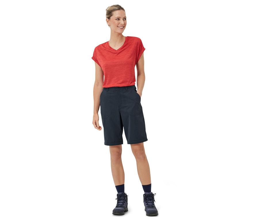 Nő áll piros pólóban és sötétkék 2 az 1-ben funkcionális nadrágban.