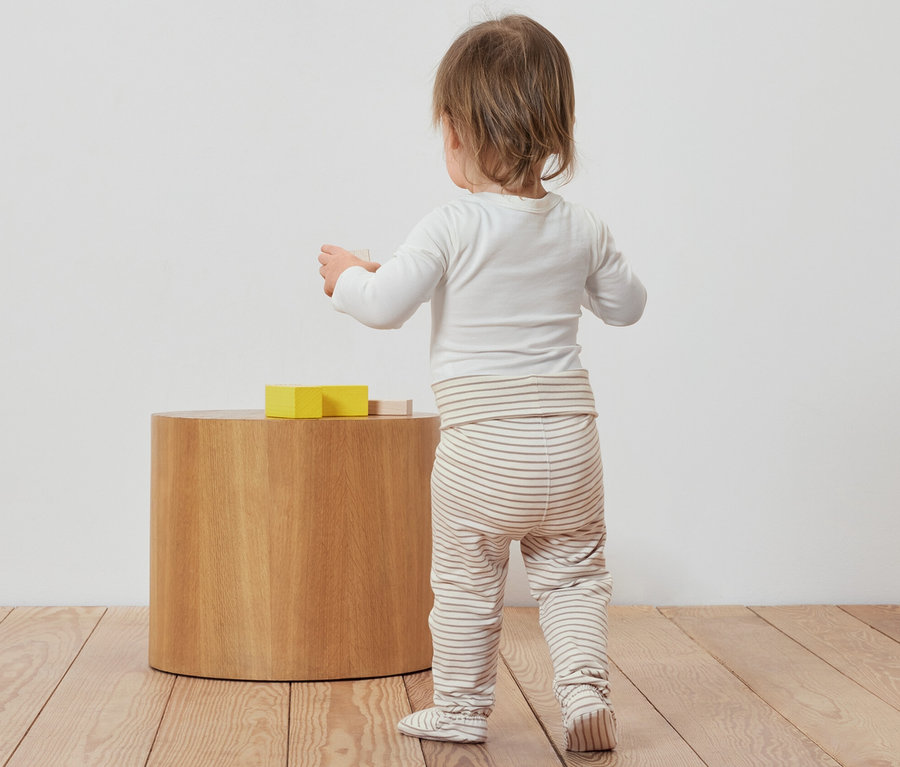 Kisgyermek háttal áll és játékokkal játszik a 3 rugdalózó kisgyerekeknek mellett.