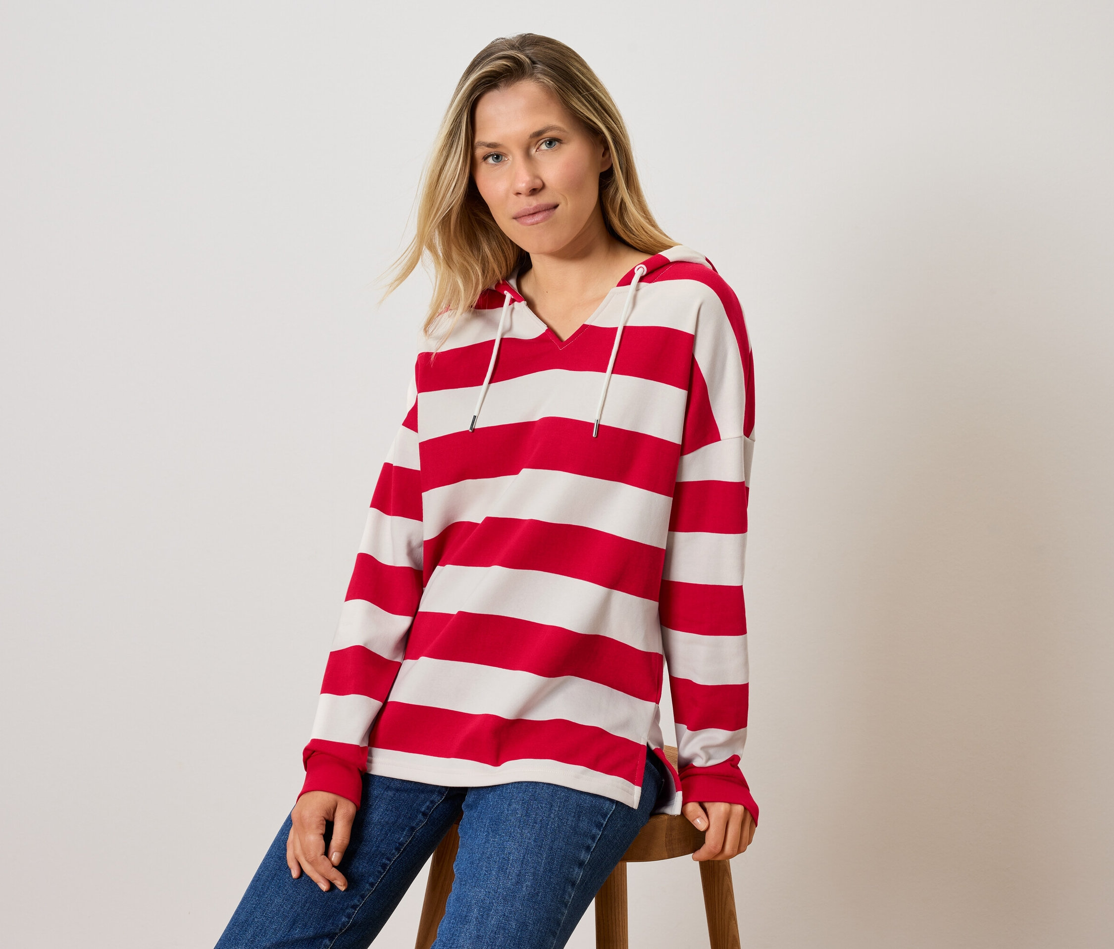 Egy nő ül egy széken, csíkos kapucnis felsőt és farmert visel.