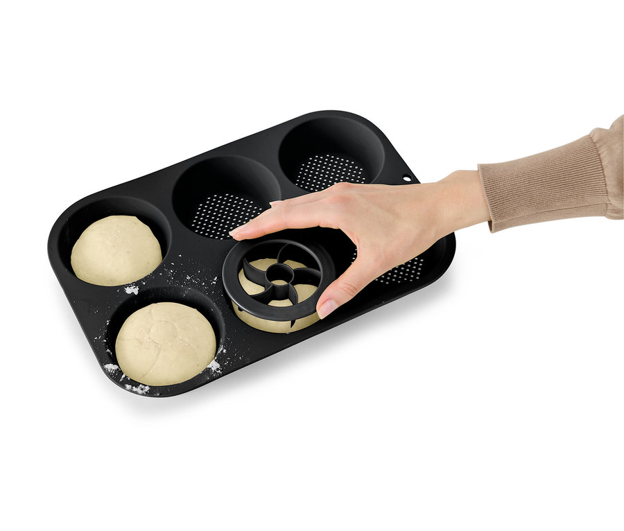 Egy kéz nyom egy kiszúrót tésztába egy fekete muffin sütőformában.