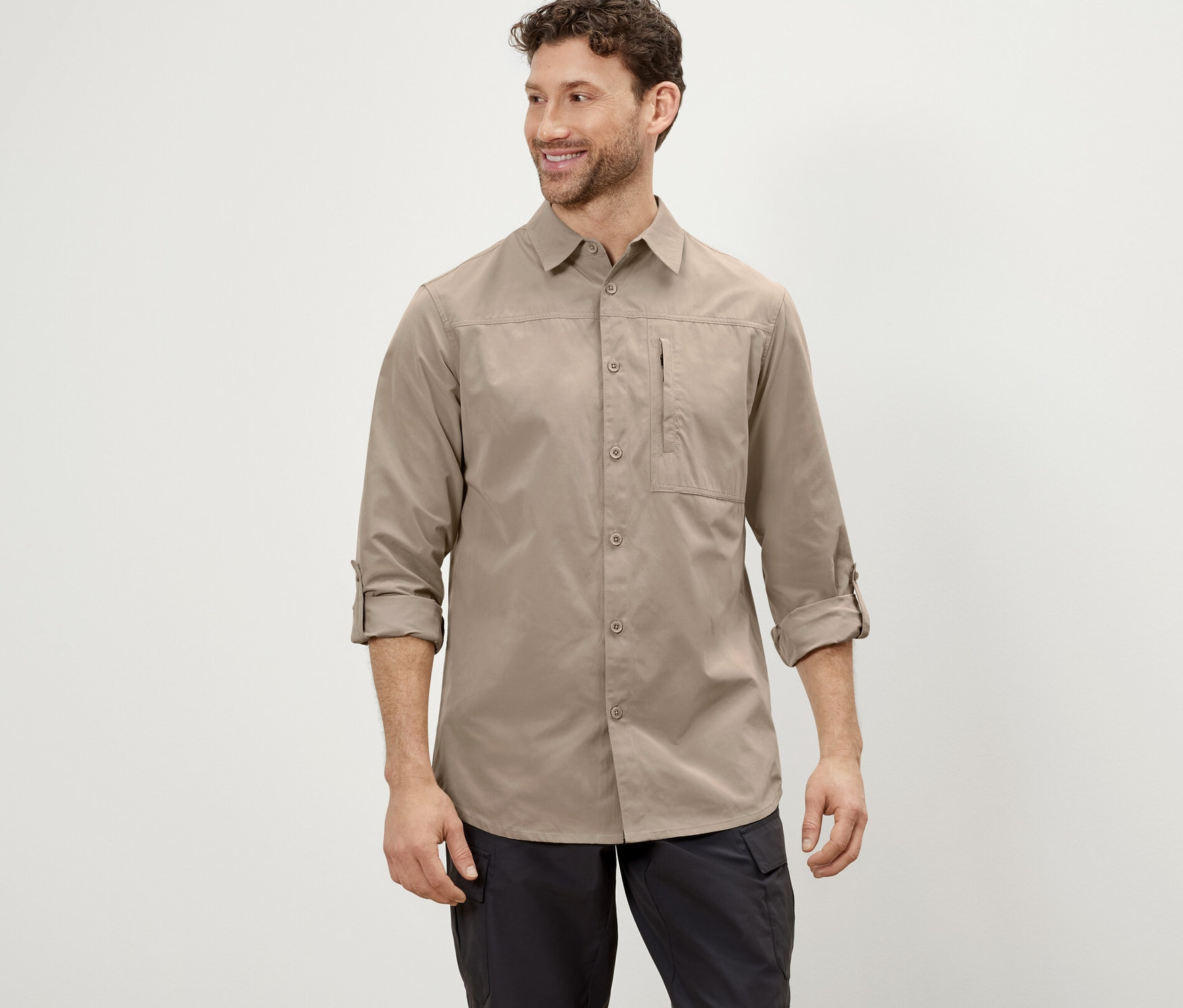 Egy férfi bézs színű, szúnyogok elleni védelemmel ellátott túraingben és fekete nadrágban pózol.