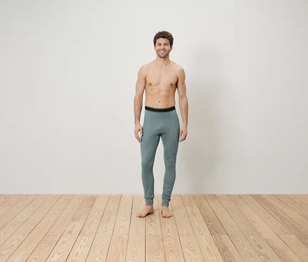 Egy felsőtest nélküli férfi áll egy fapadlón, szürke leggingset visel.