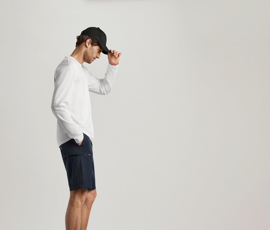 Fekete sapkás és tengerészkék rövidnadrágos férfi fehér 2 Langarmshirts-et visel.