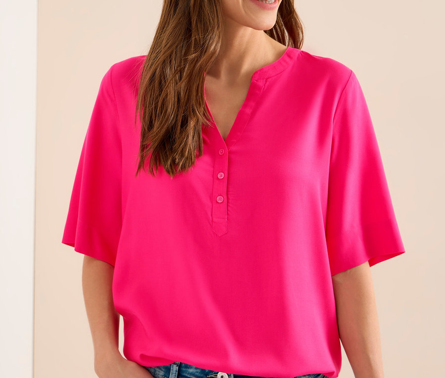 Farmerben lévő nő rózsaszín CECIL tunikablúzt visel.