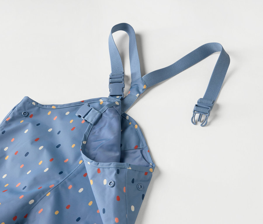 Kék gyerek kötény színes pöttyökkel és kék pántokkal fehér háttér előtt.