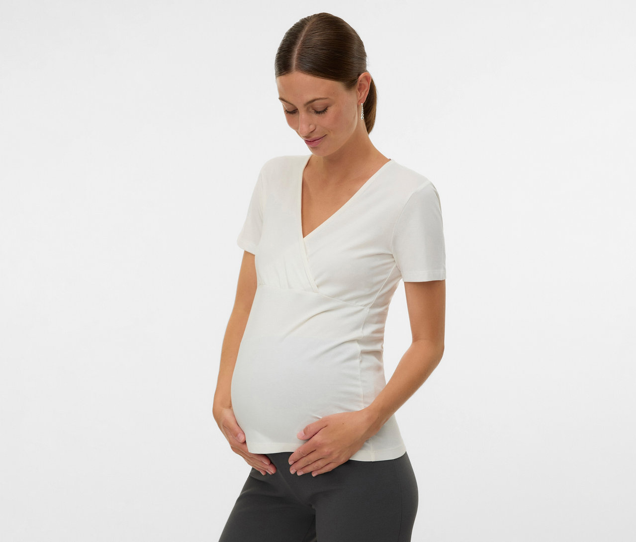 Egy terhes nő fogja a hasát, és egy fehér 2 db MAMALICIOUS kismama felsőt visel.