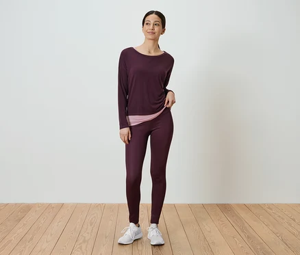 Egy nő áll, és bordó, hosszú ujjú inget és bordó leggingset visel.