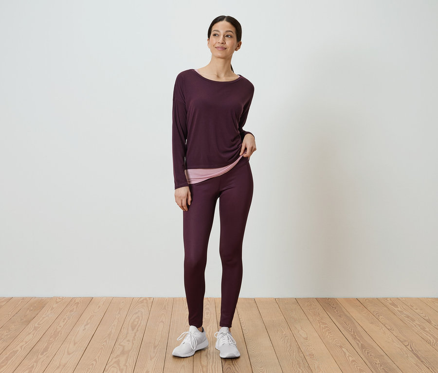Egy nő áll, és bordó, hosszú ujjú inget és bordó leggingset visel.