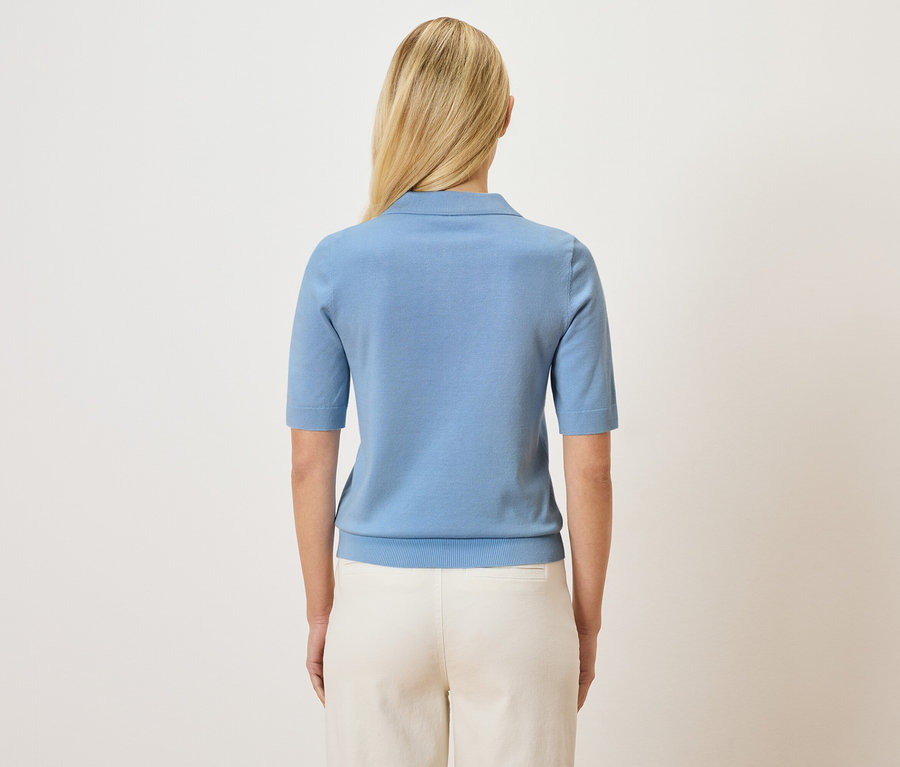 Hátulnézet egy szőke hajú nőről, aki világoskék pólót és világos nadrágot visel.