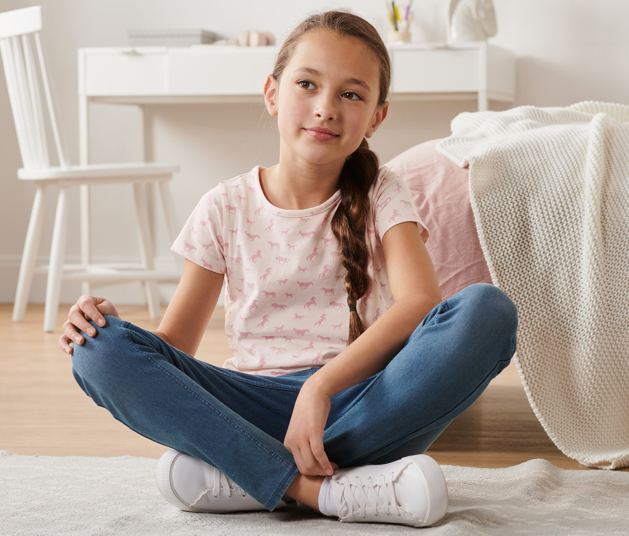 Lány ül a földön, lovas mintás póló van rajta. A szettben 2 lány póló van, rózsaszín és sötétkék.