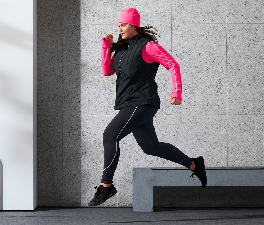 Nő fut funkcionális steppelt termomellényben, sportnadrágban, neonpink termosapkában és neonpink funkcionális felsőben.