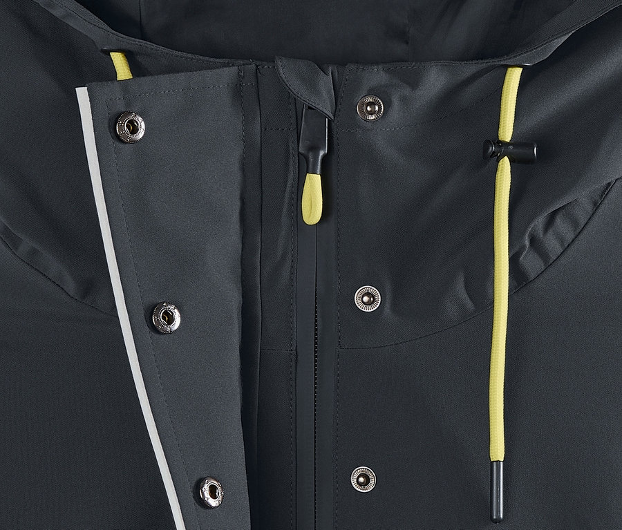 Egy sötétszürke női funkcionális parka esőkabát részlete, a cipzár és a patentok láthatók.