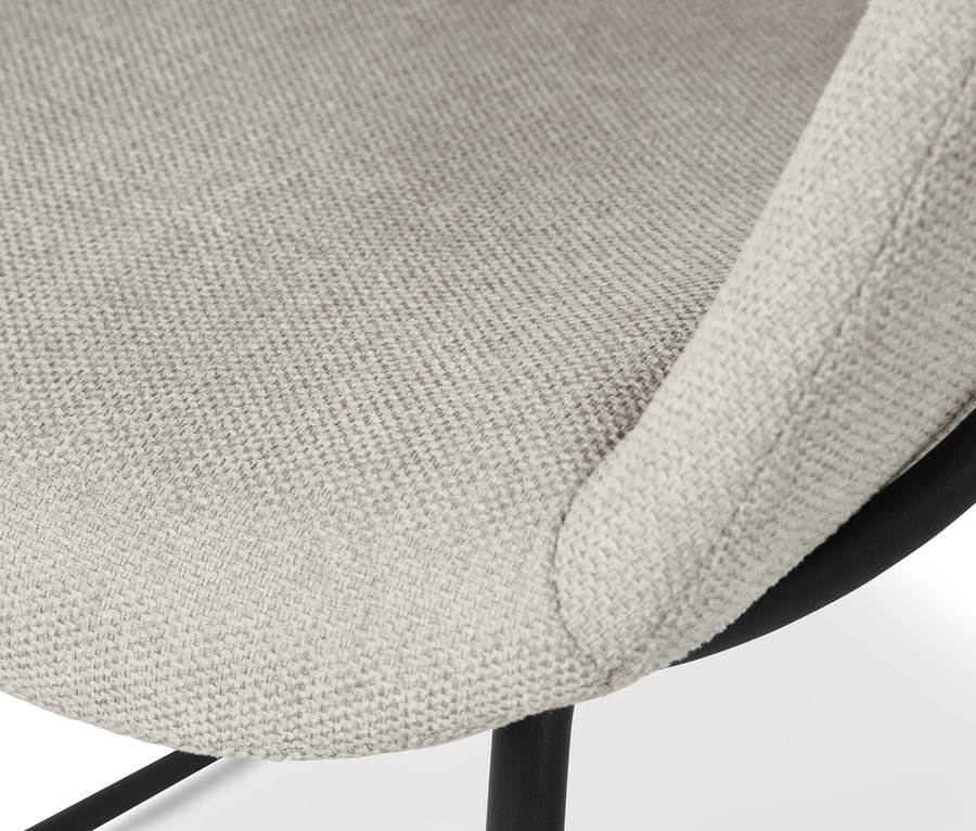 Egy bézs kárpitozott kagylószék részlete fémlábakkal.