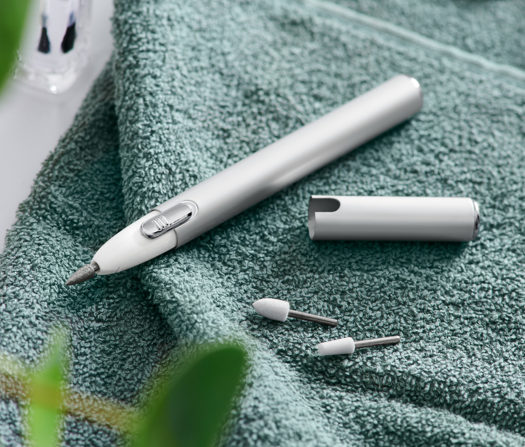 Egy manikűr-pedikűr készlet zöld törölközőn fekszik tartozékok, egy reszelő és egy olló mellett.