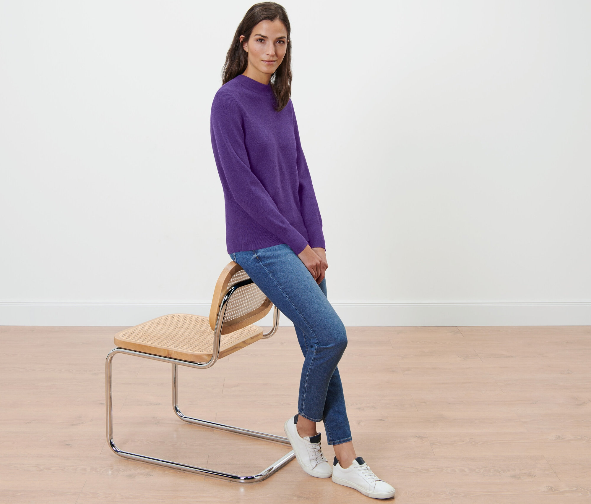 Egy nő ül egy széken, és lila, finomkötésű női pulóvert visel.