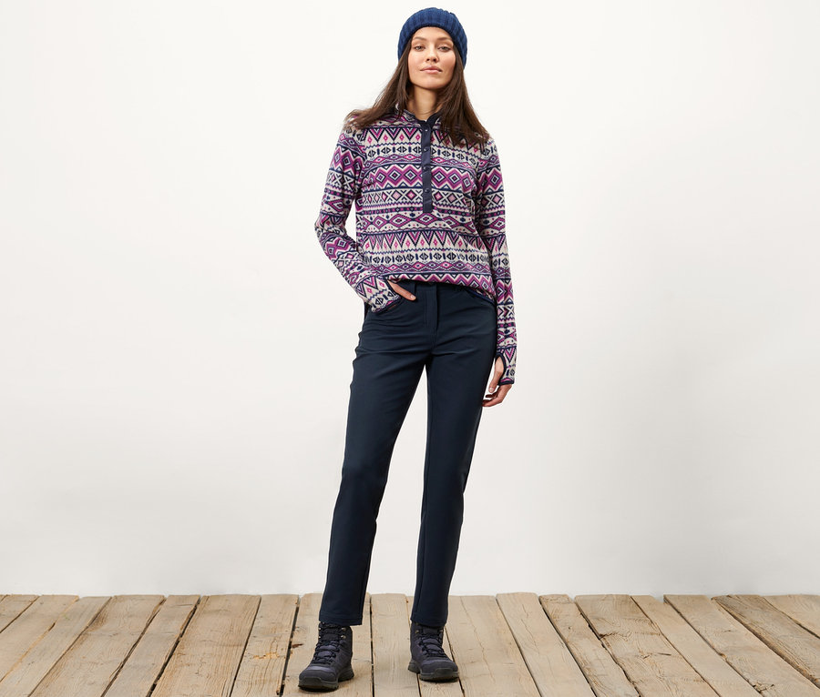 Nő pózol termonadrágban, mintás pulóverben és sapkában.