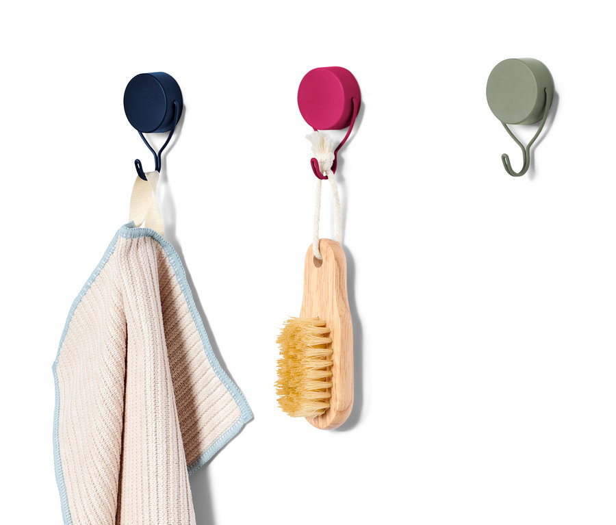 Három mágneses akasztó van egy fehér falon, melyeken egy törölköző és egy kefe lóg.