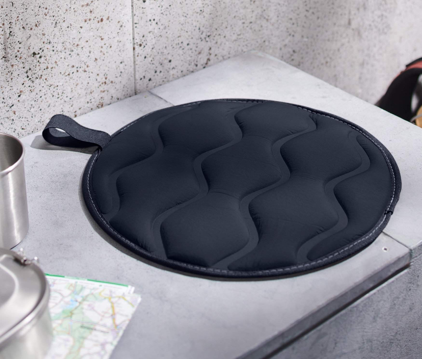 Egy szürke betonpadon egy összecsukható termo ülőpárna fekszik.