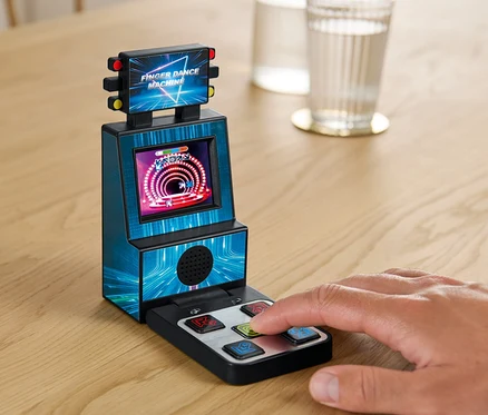 Egy kéz a Mini retro ujj táncparkett játékgépen játszik egy asztalon egy pohár víz mellett.