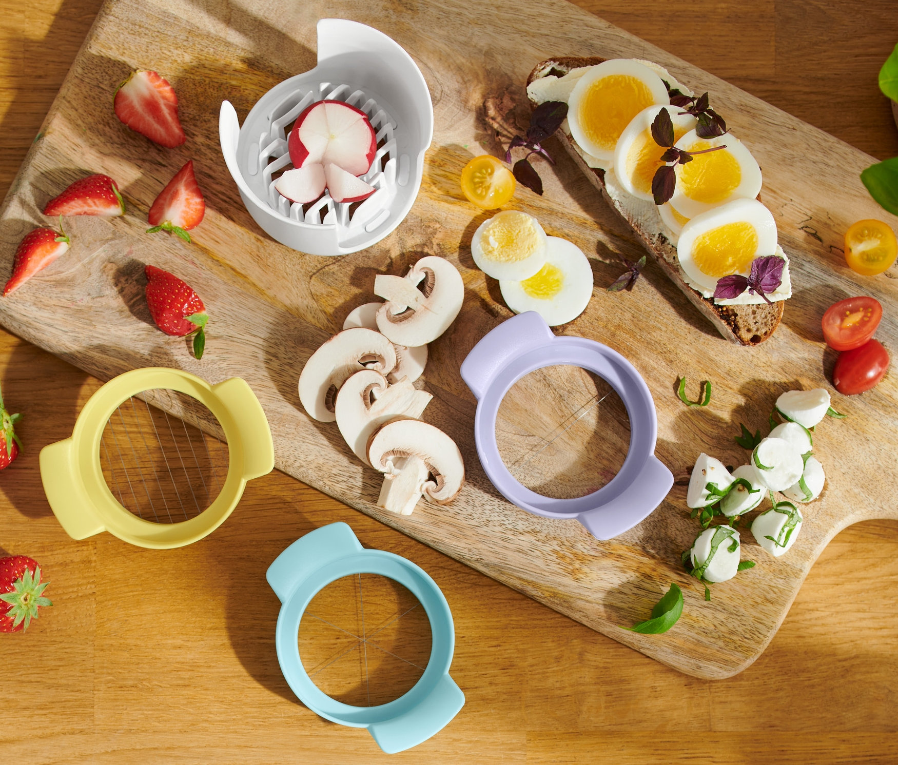 Egy fa deszkán eper, gomba, 3 az 1-ben tojásszeletelő, tojásos pirítós, mozzarella és koktélparadicsom található.