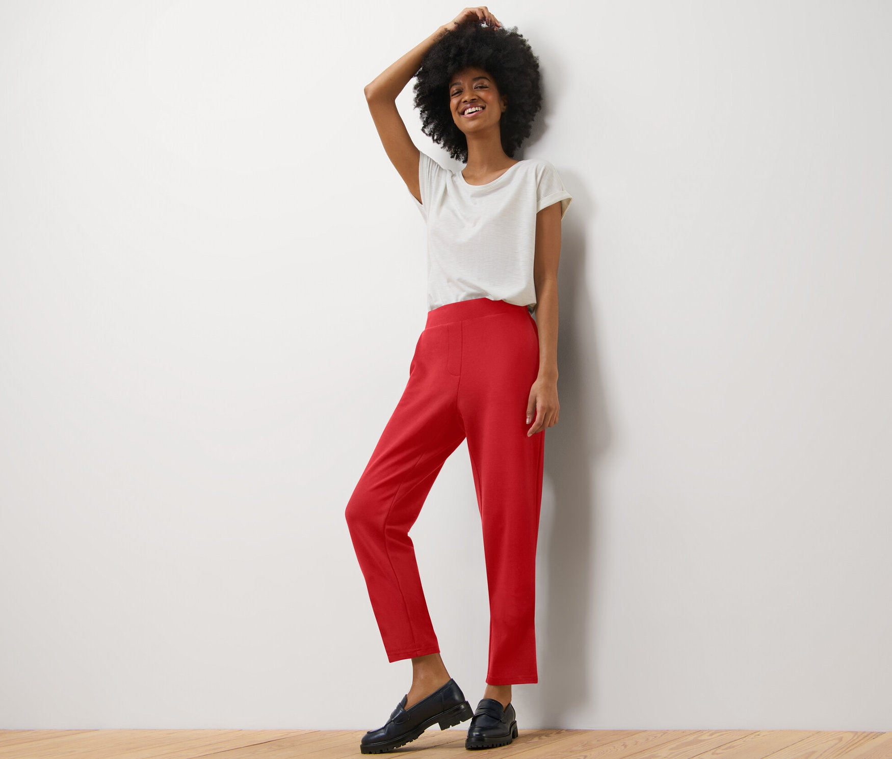 Nő pózol világos pólóban és piros női lezser nadrágban.