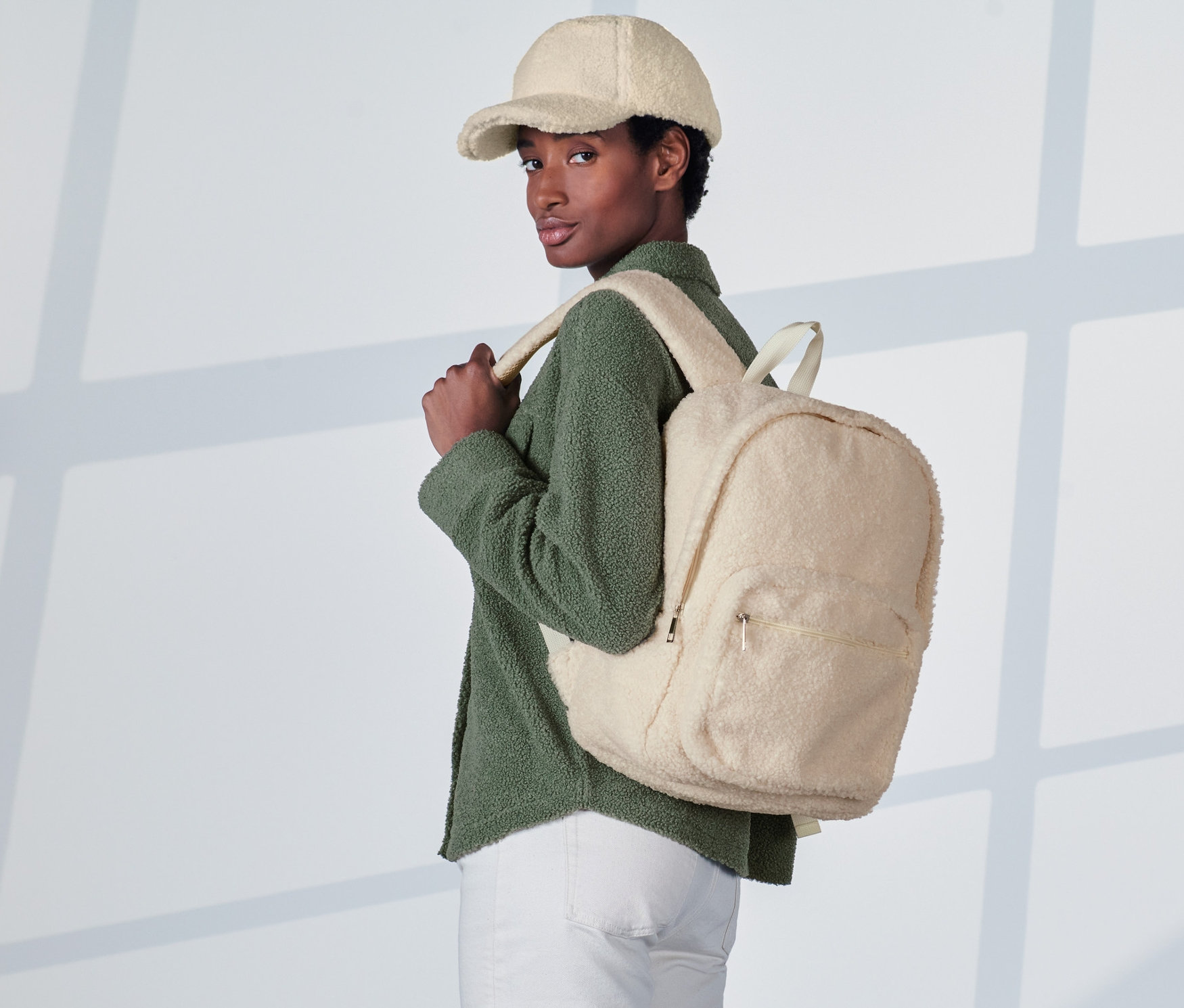 Nő krémfehér plüss hátizsákkal és krémfehér baseball sapkával.