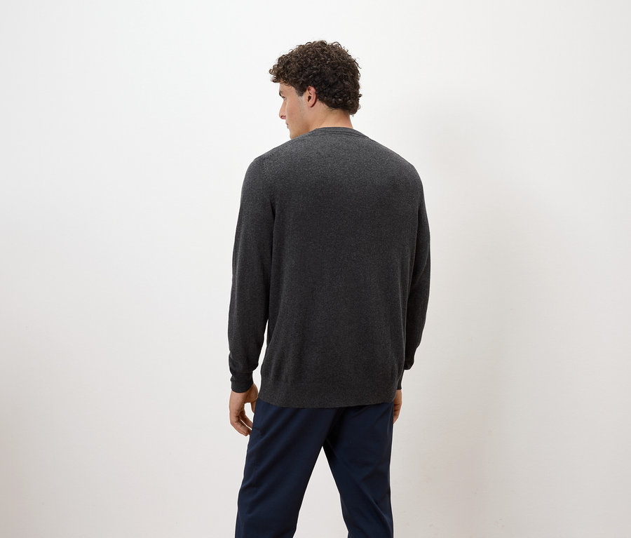 Egy göndör hajú férfi háttal áll, szürke pulóvert és kék nadrágot visel.