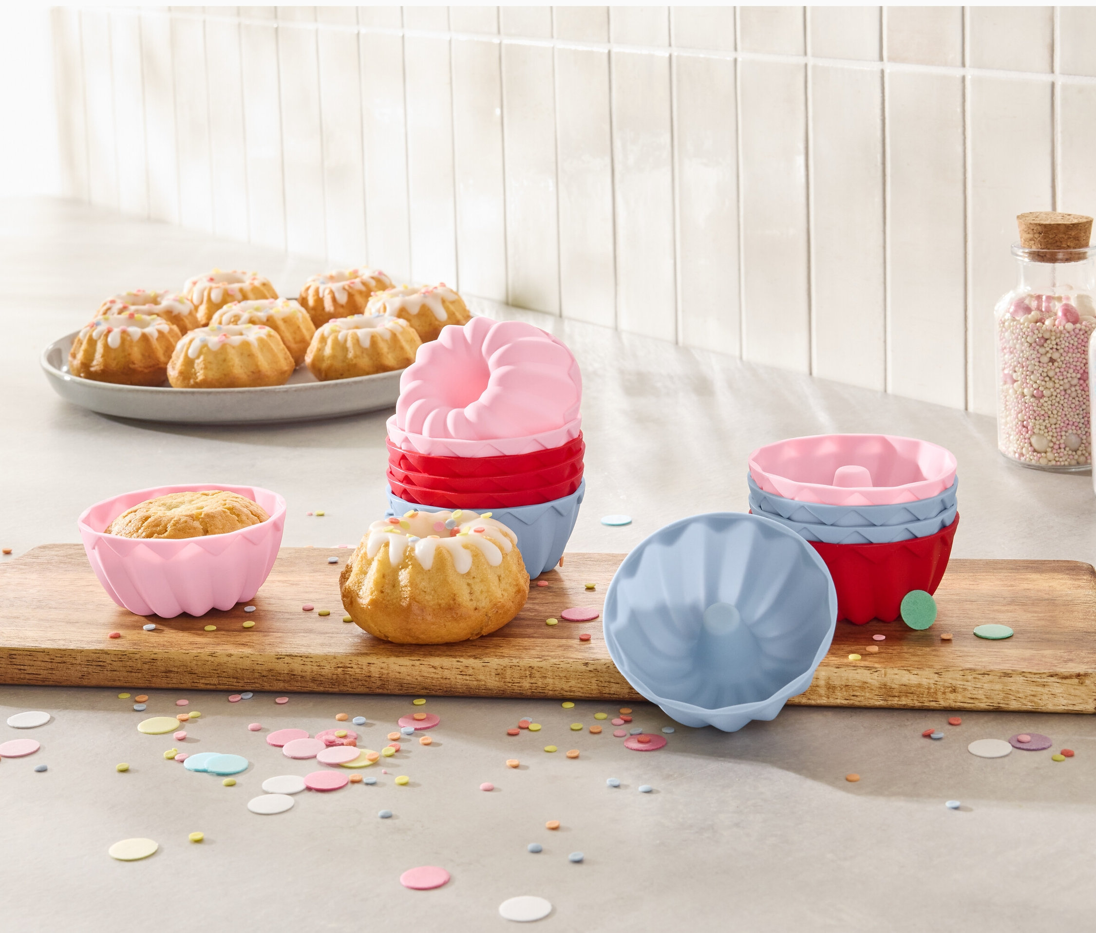 Mini kuglófok egy tányéron és 12 mini kuglóf sütőforma egy fa deszkán.