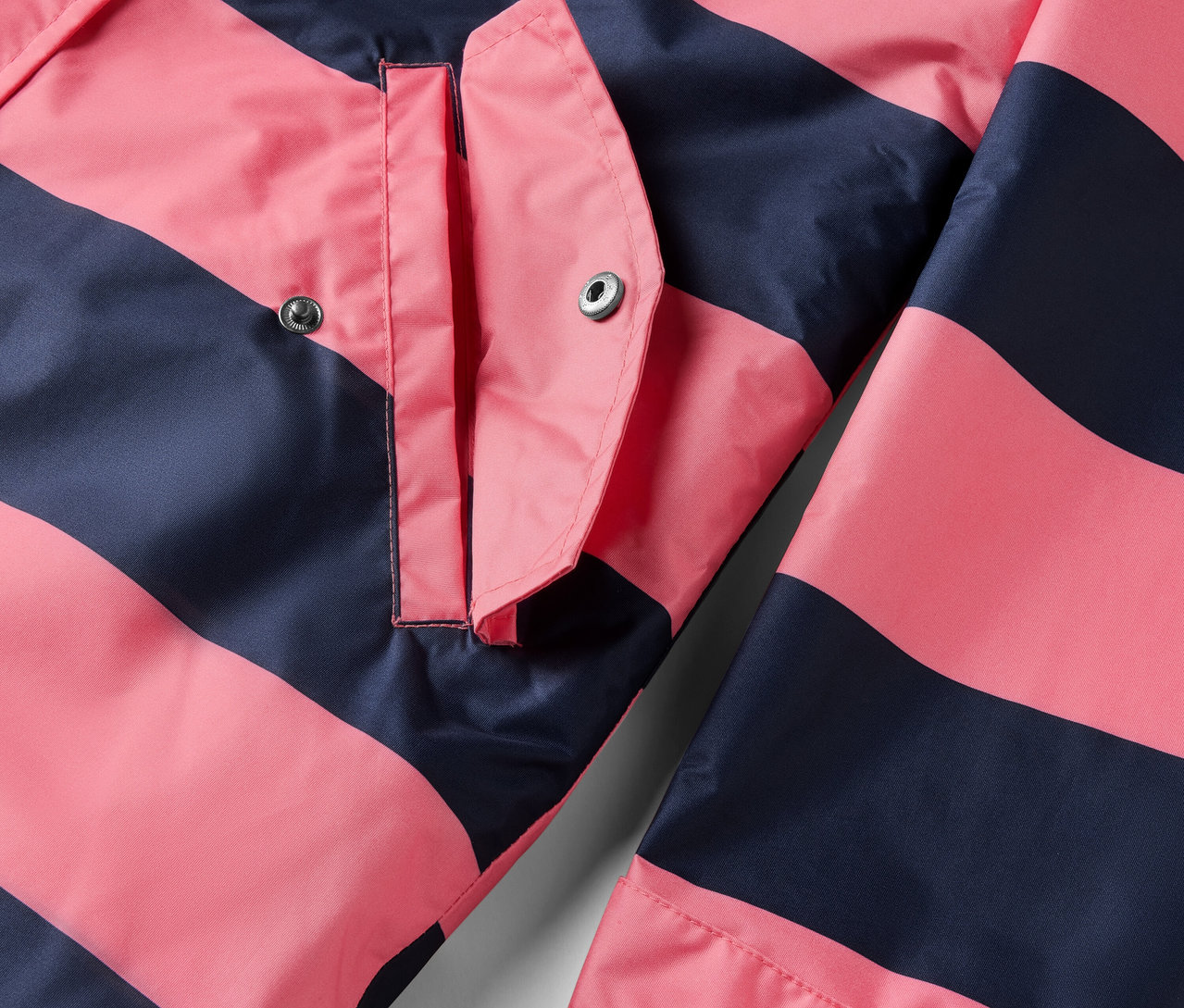 Egy rózsaszín és sötétkék csíkos, 3 az 1-ben esőkabát részlete egy zsebbel.