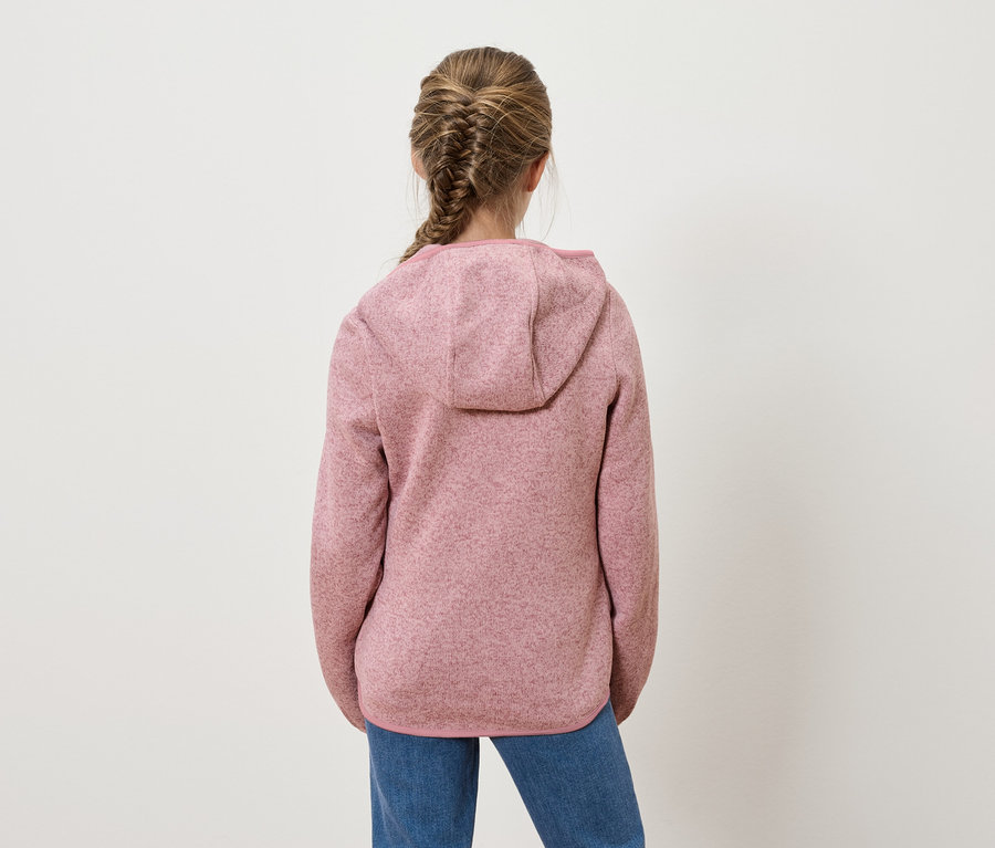 Egy copfos lány háttal áll a kamerának, rózsaszín kapucnis pulóvert és farmert visel.