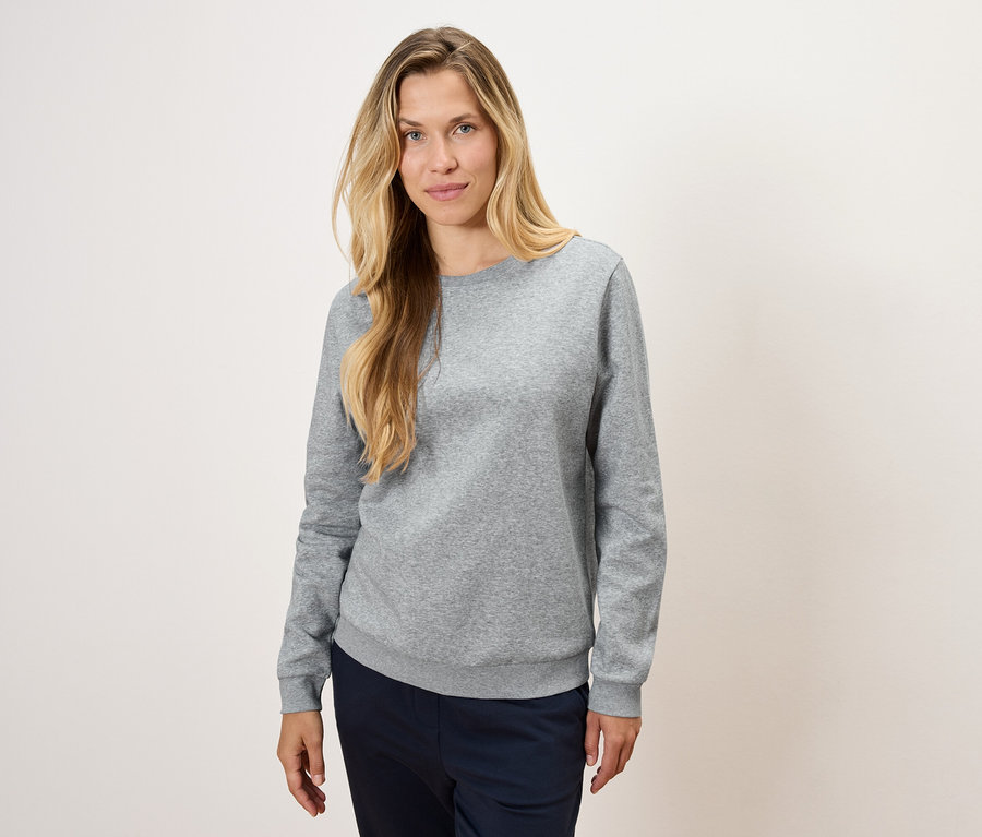 Egy nő szürke pulóvert és sötétkék nadrágot visel.