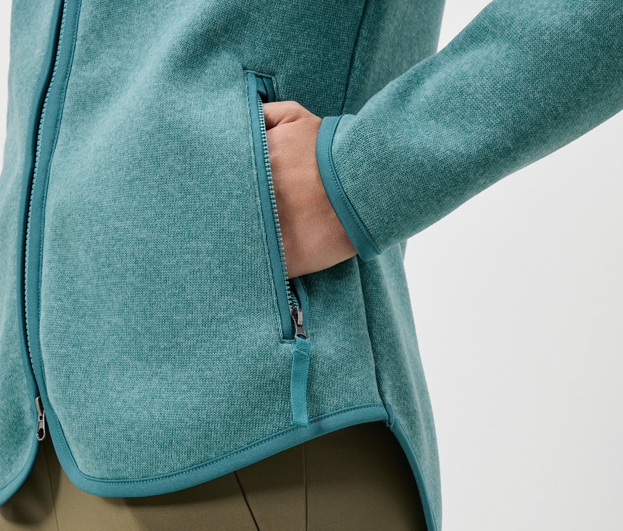 Egy türkiz fleece kabát közeli képe, kéz a zsebben.
