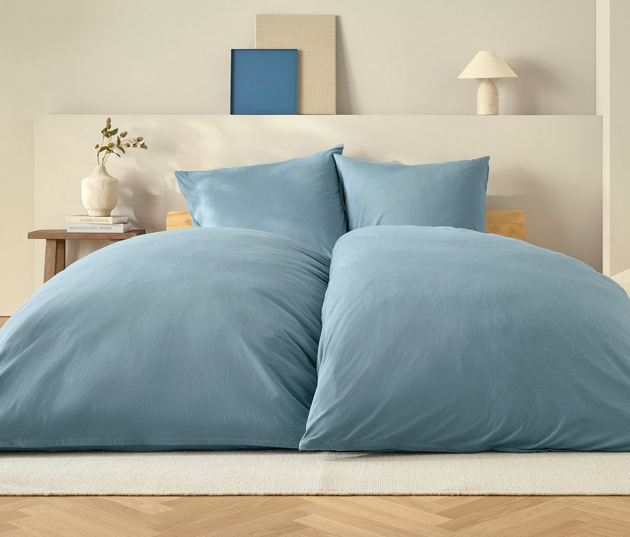 Kék paplan és két párna egy ágyon, fehér szőnyegen.